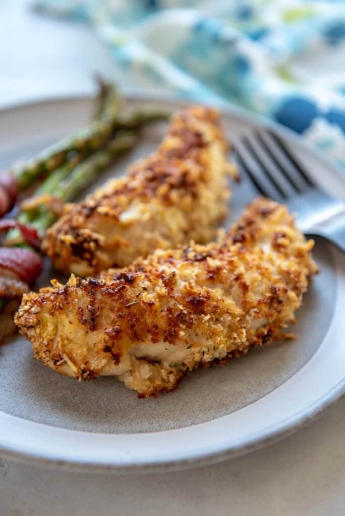 Close up photo of air fryer chicken tenders with asparagus in the background