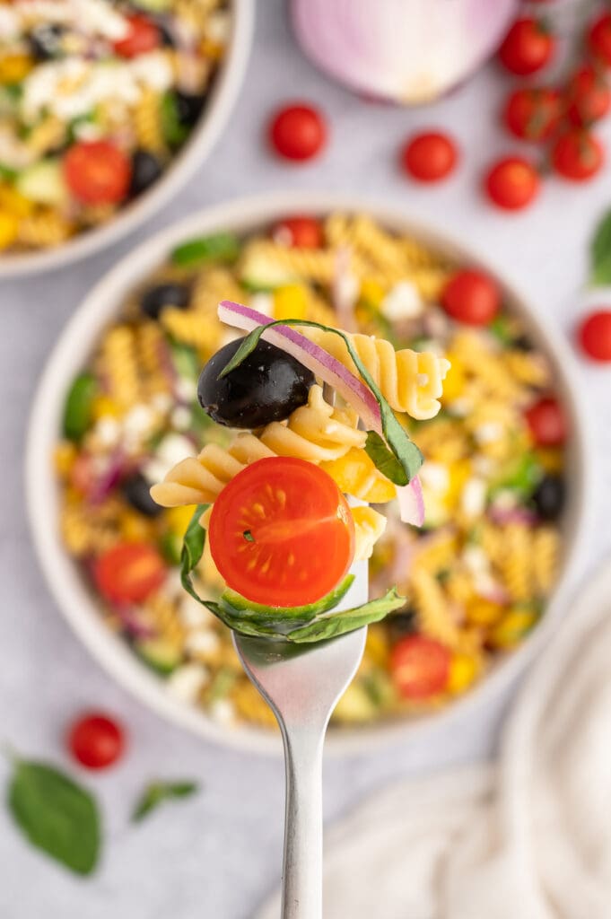 a close up picture of balsamic pasta salad on a fork with the bowl in the background