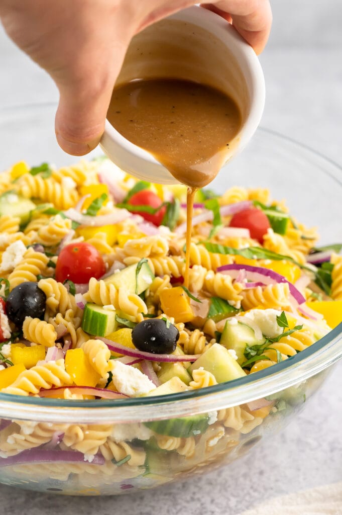 a glass bowl filled with balsamic pasta salad and a woman pouring balasamic dressing over it