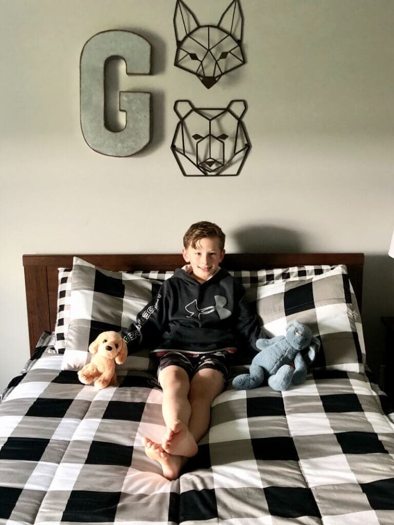 A boy smiling on top of his beddy's bed.