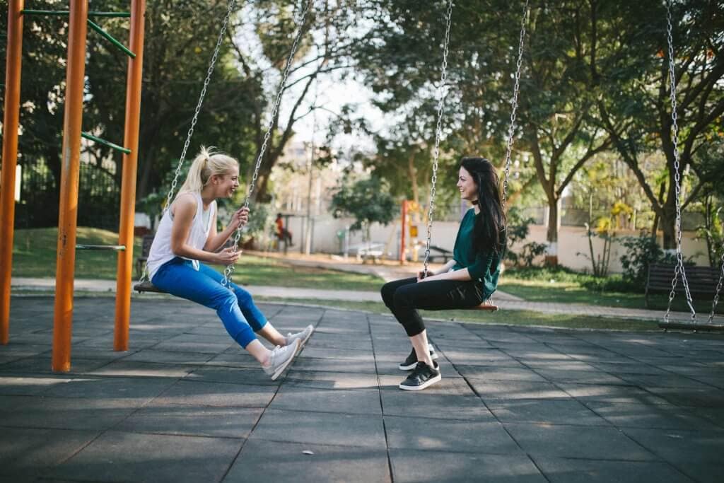 Two girls on swings talking and laughing