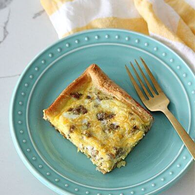 Piece of breakfast casserole on a teal plate with a gold fork and a white and yellow napkin