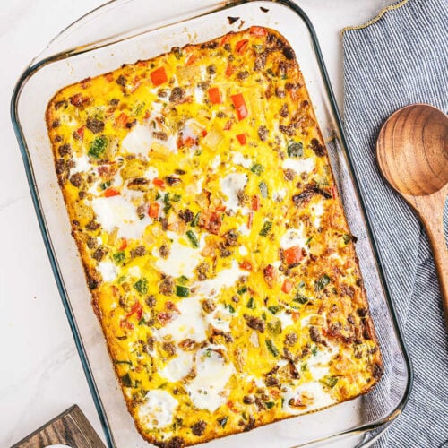 a 9x13 pan filled with breakfast casserole with eggs and a wooden spoon and grey napkin