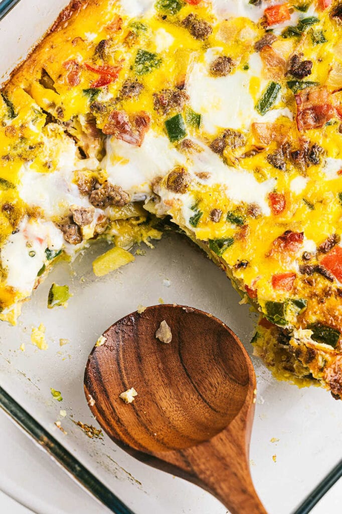 Breakfast casserole dish in a glass pan with a portion of it taken out with a wooden spoon