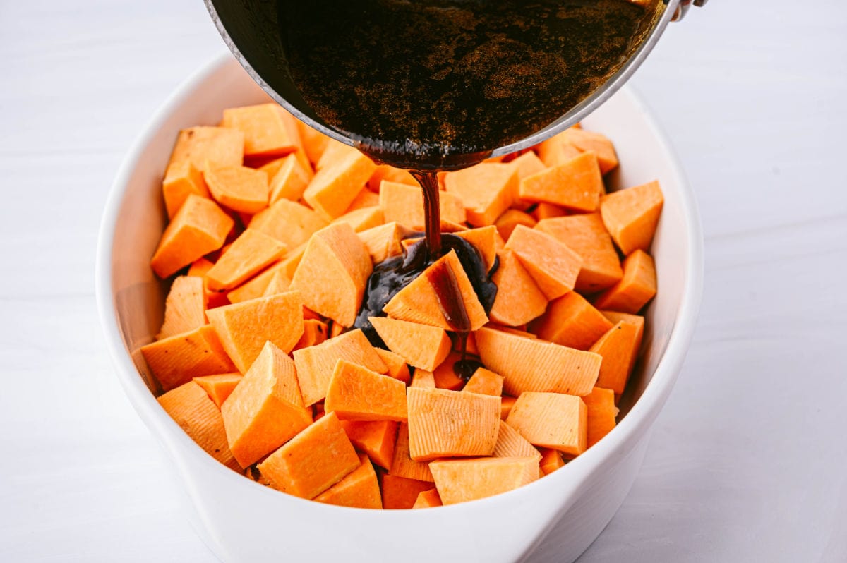 baking dish filled with raw sweet potatoes and the sauce mix being poured on top of them