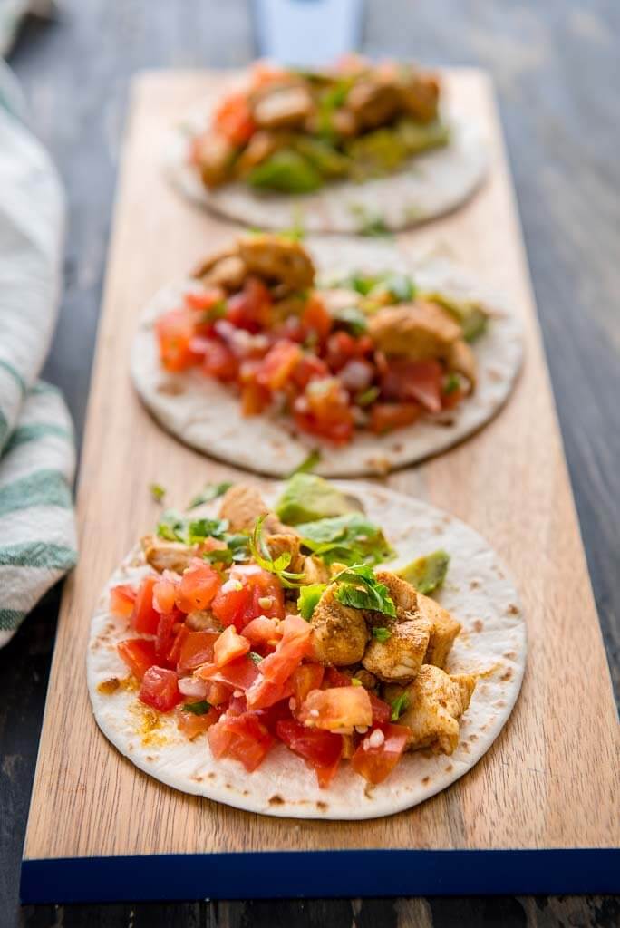 Photo of 3 cajun chicken street tacos on a wooden platter. The first taco is in focus and the other two are out of focus.