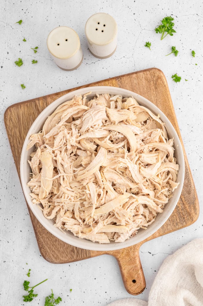 a bowl of shredded chicken on a wooden cutting board