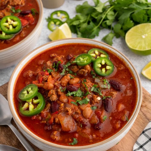 a bowl of chili with jalapenos on the top and cilantro in the background