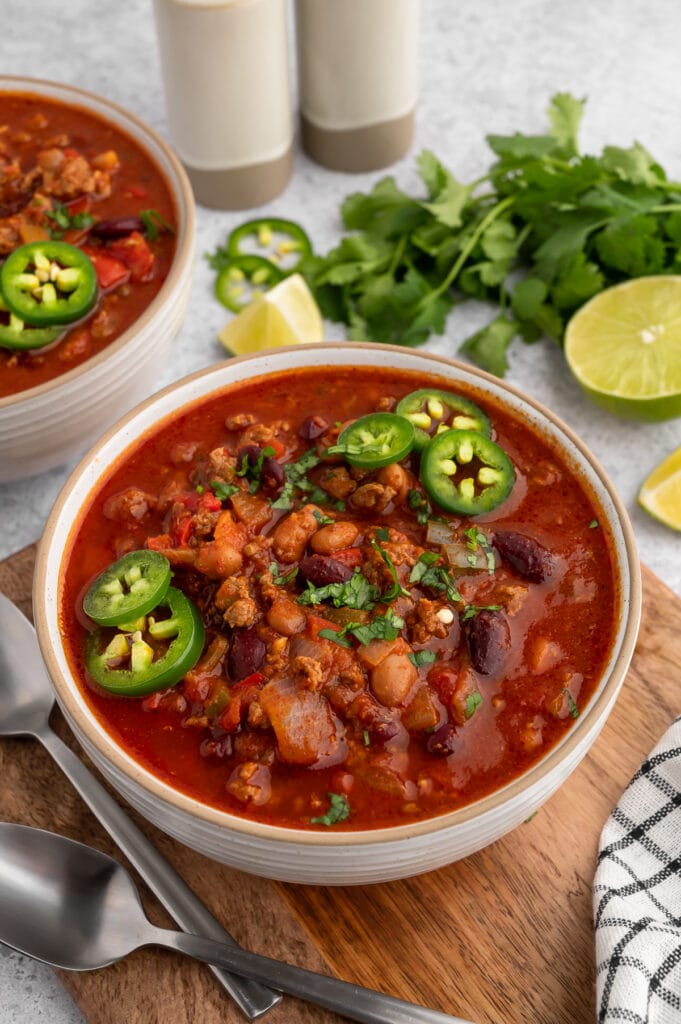 a bowl of chili with jalapenos on the top and cilantro in the background