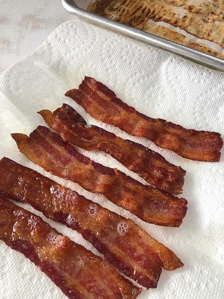 4 pieces of bacon on a paper towel with the pan behind it.