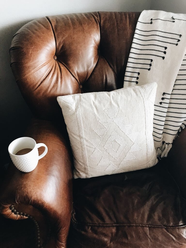 Brown chair with blankets and a pillow and coffee cup.