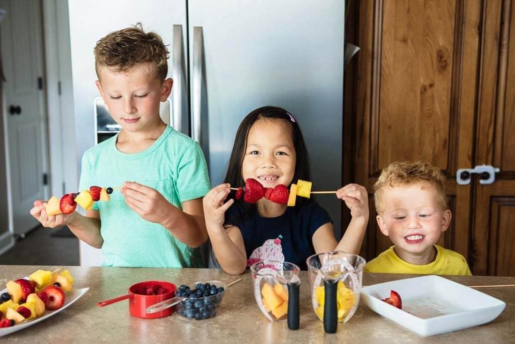 Two boys and a girl making fruit skewers