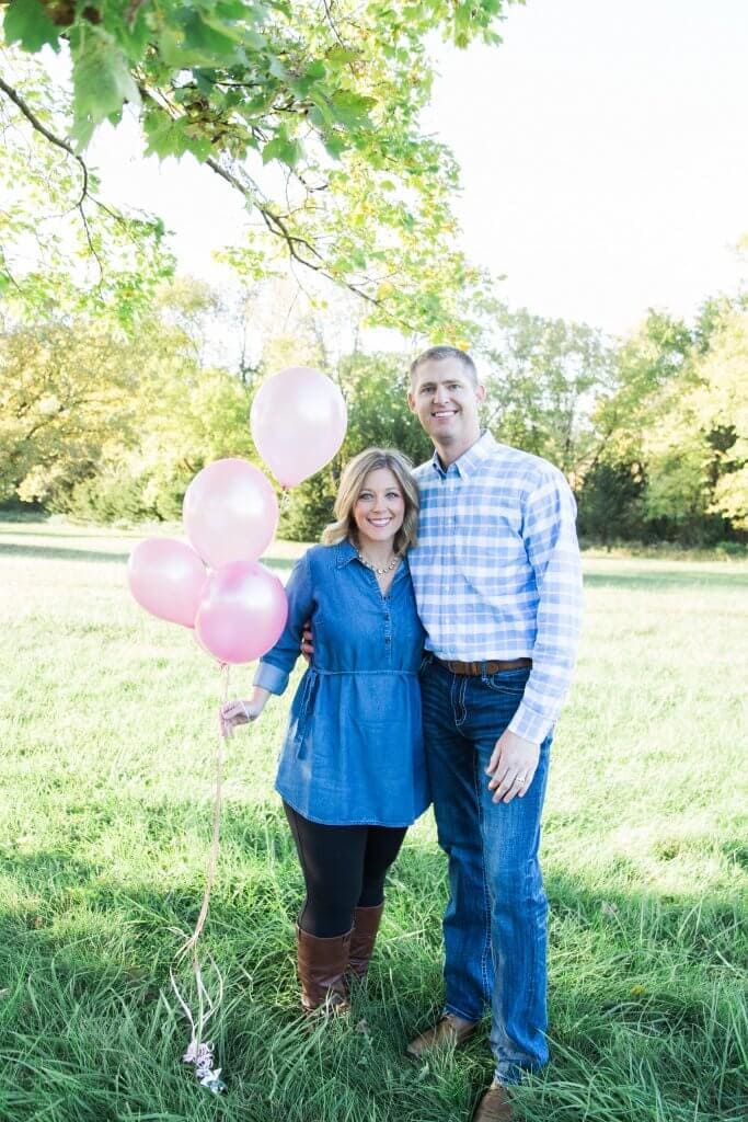A woman and man holding pink balloons because they are pregnant with a baby girl