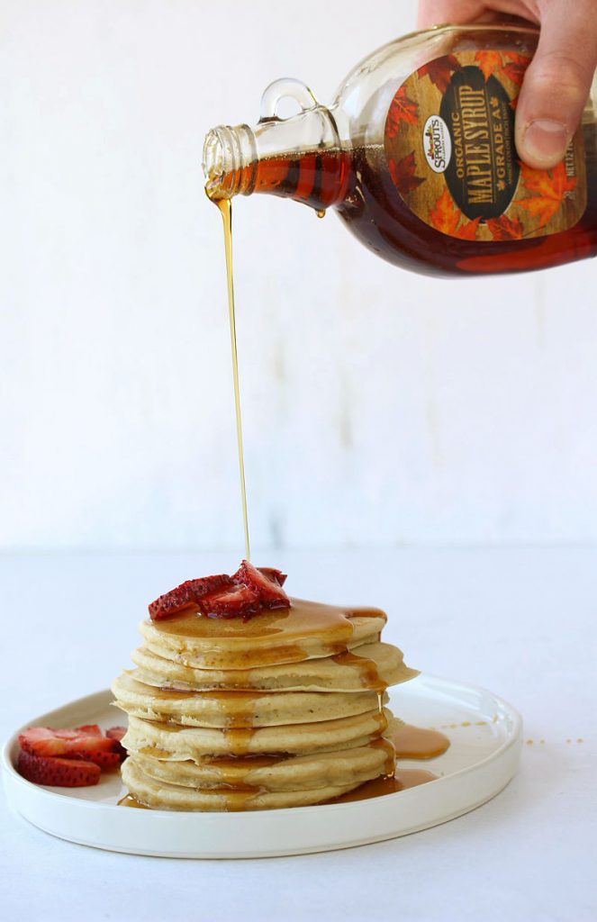 A person pouring maple syrup on a stack of pancakes