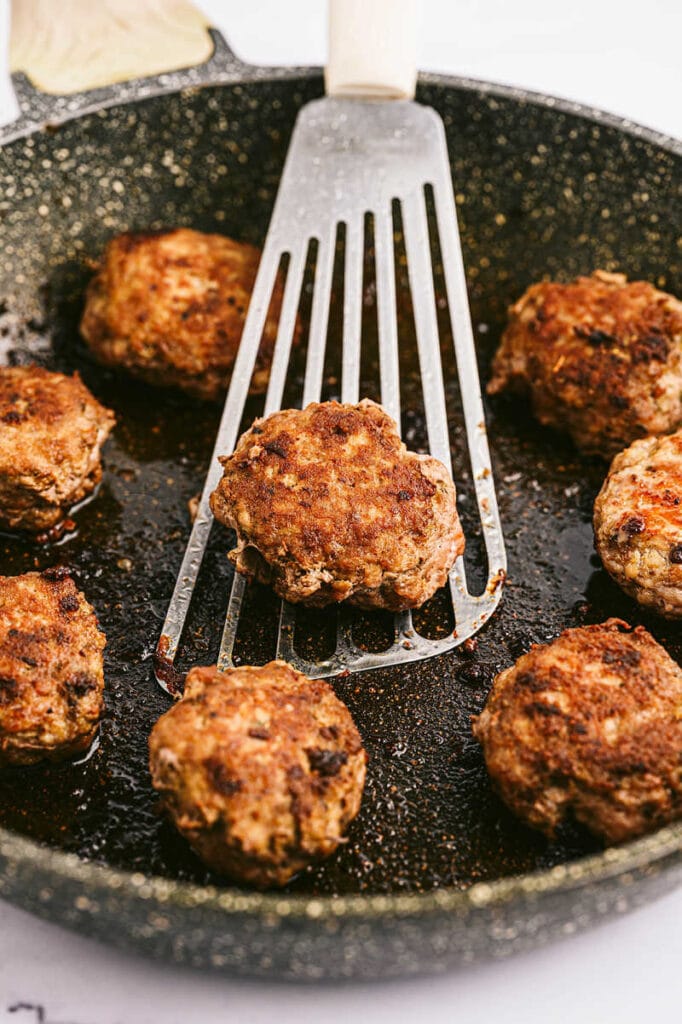 a skillet with homemade sausage patties and a spatula holding one