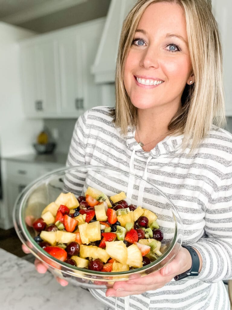 a woman in a grey and white striped shirt holding a bowl of fresh fruit