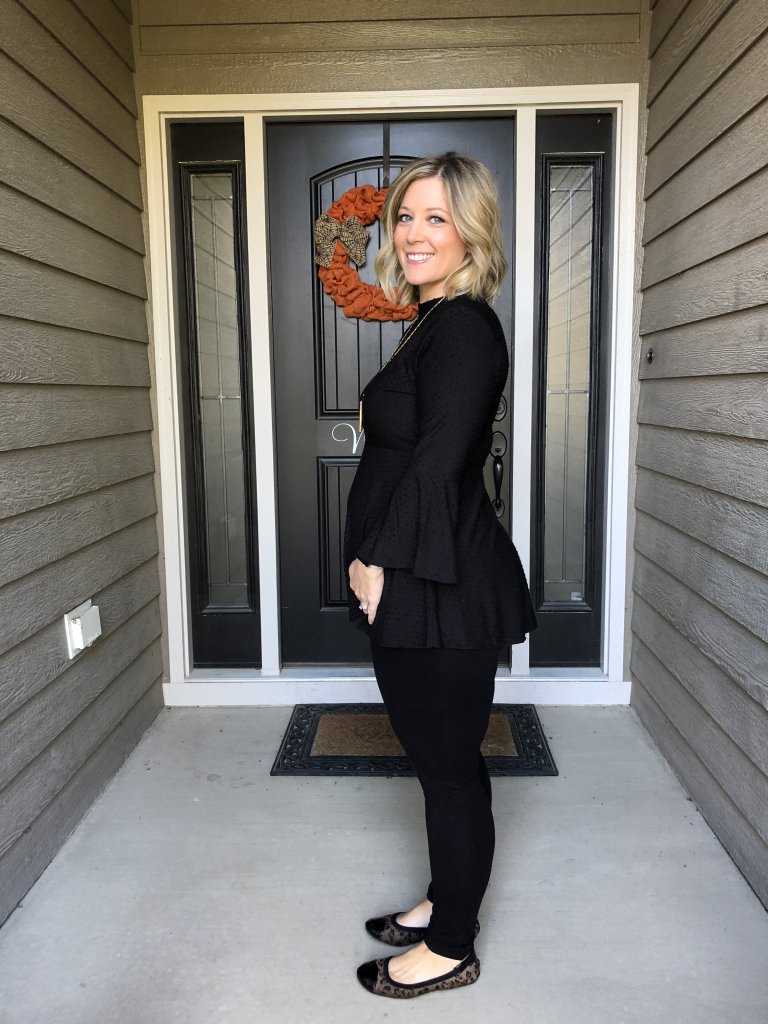 A woman in all black showing her pregnant belly