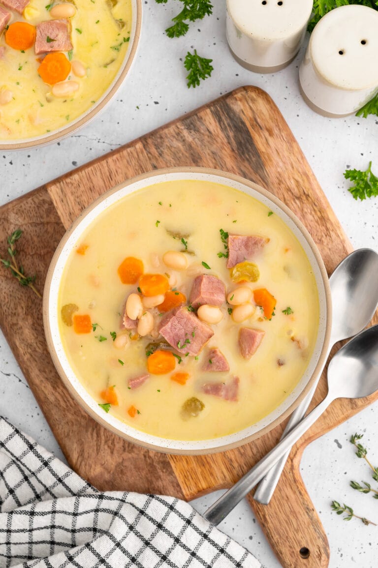 a bowl of creamy ham and bean soup on a wooden cutting board