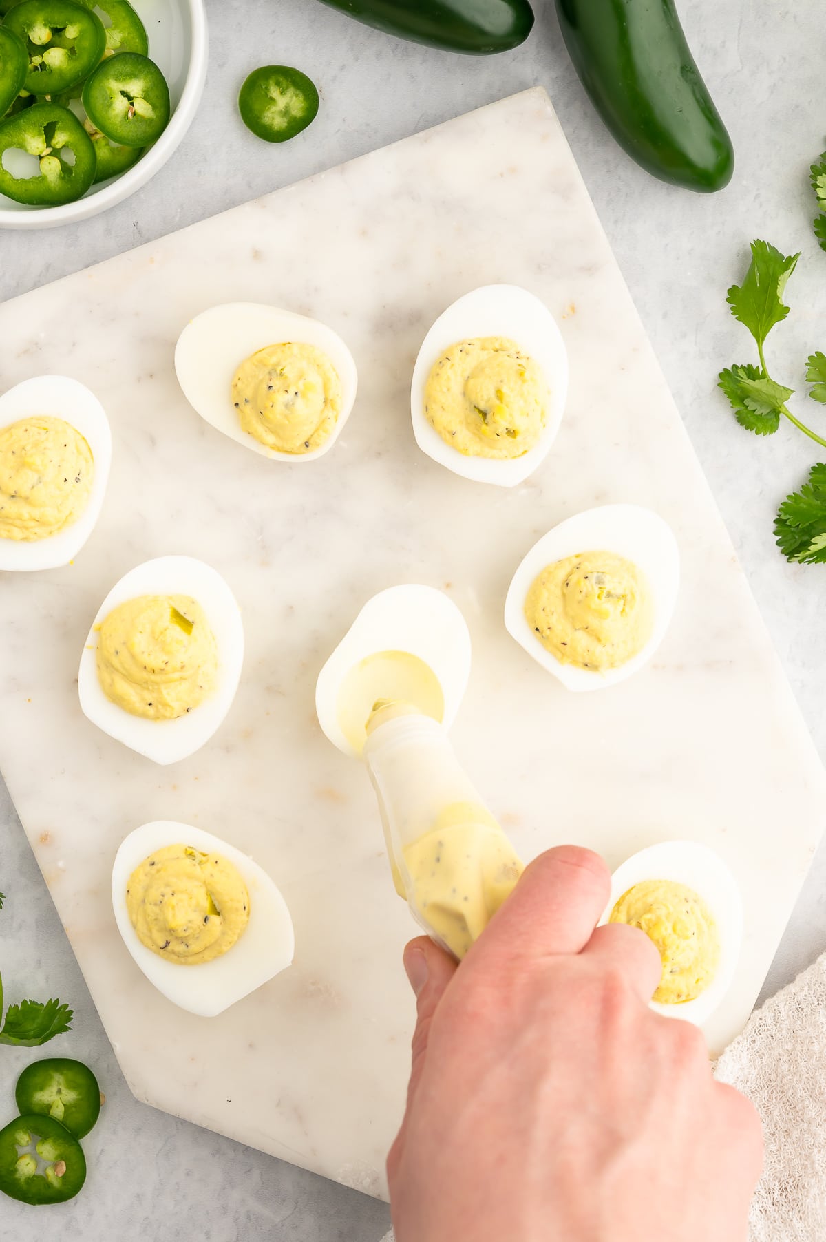 a woman using a piping back to fill her deviled eggs
