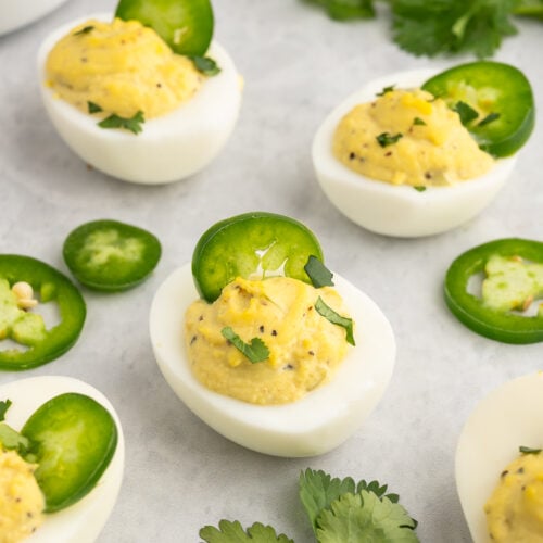 a white plate covered with deviled eggs with jalapenoes on top and cilantro