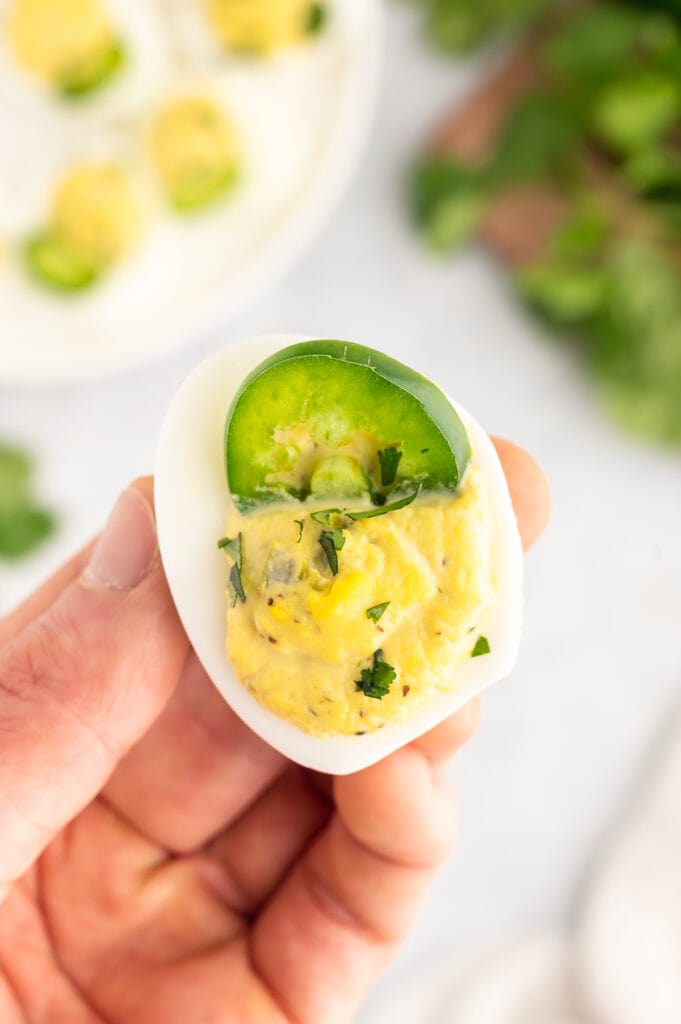 a woman holding one jalapeno deviled egg up close