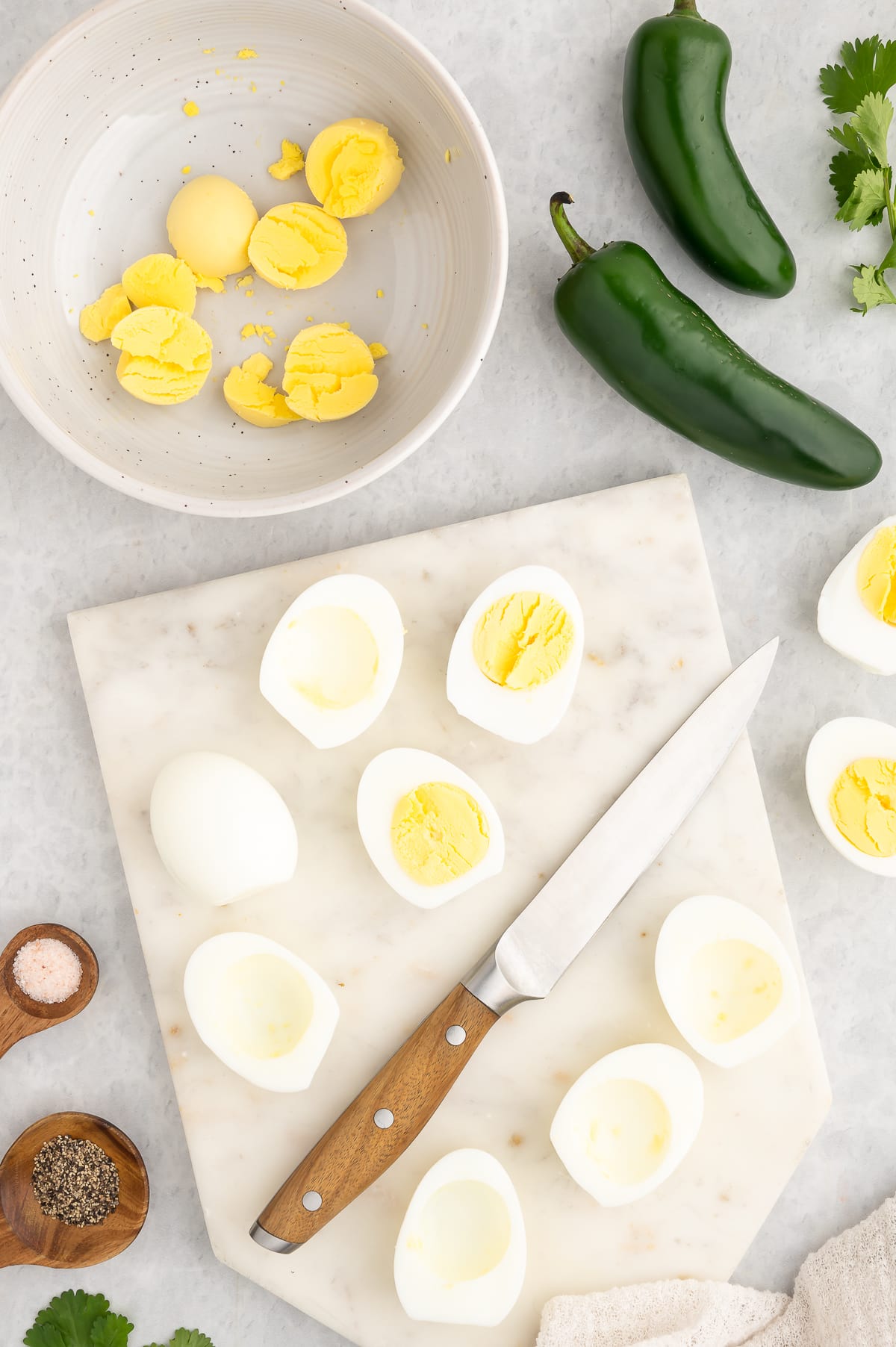 a cutting board with knife with all the eggs cut and some of the yolks placed in a bowl