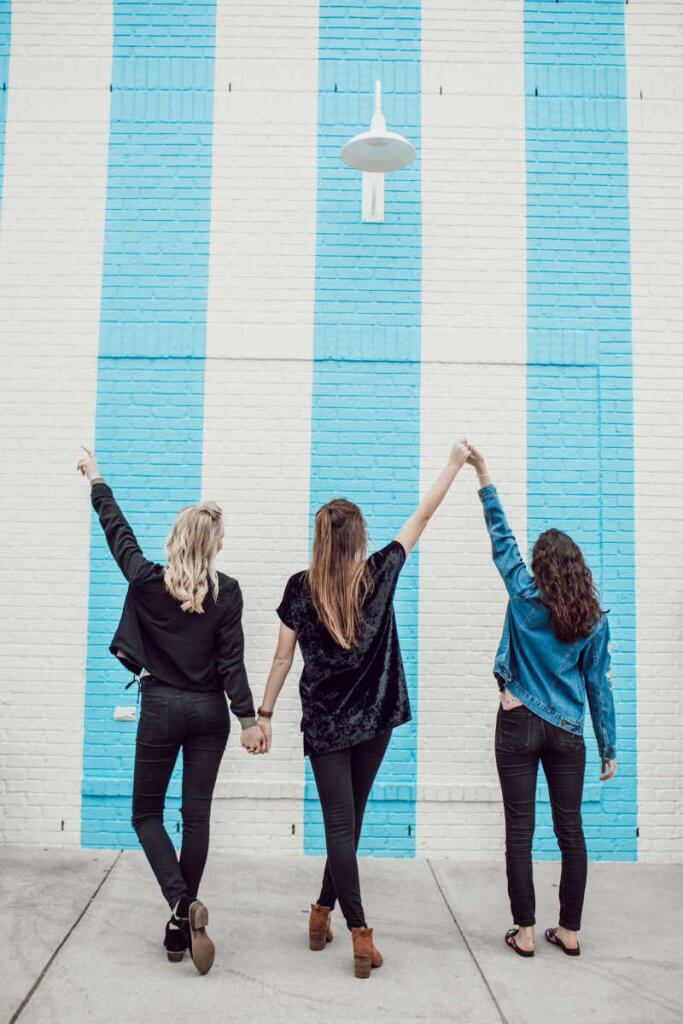 3 girls with their back turned to the camera with a blue stripe wall