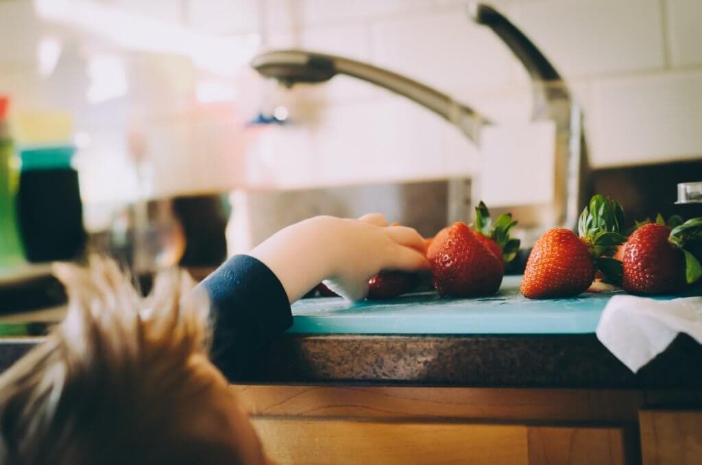 little boy reaching for strawberries on the counter