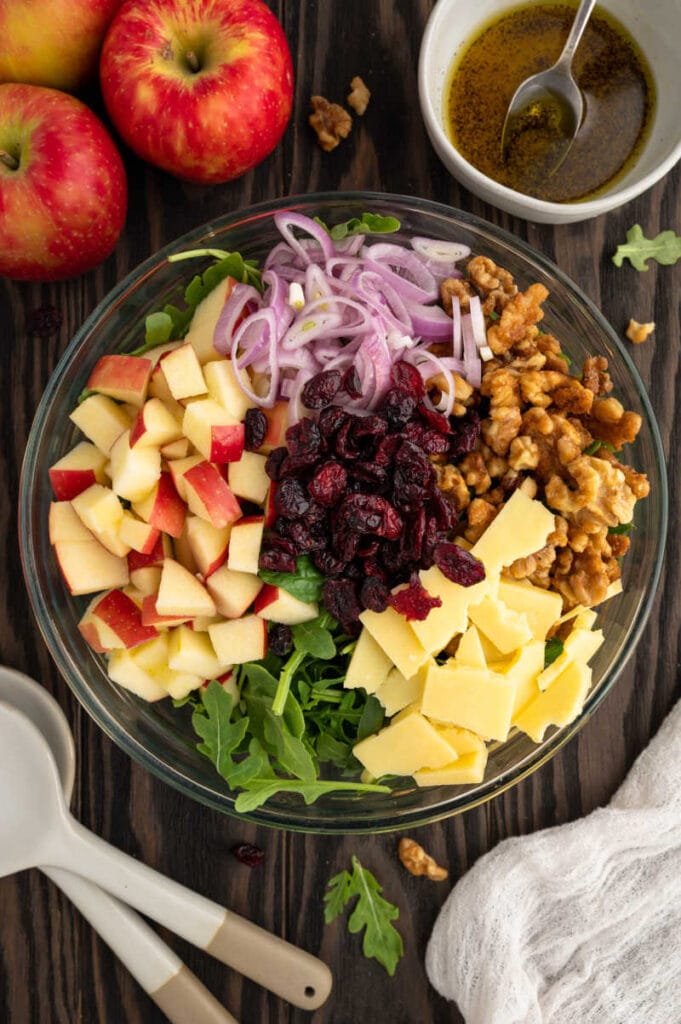 a bowl with all the ingredients for the apple walnut salad.  Arugula, cheese, walnuts, cranberries, shallot, apples