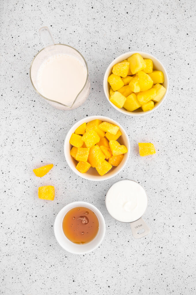 aerial view of the ingredients for mango pineapple smoothie including almond milk, pineapple, mango, honey, yogurt
