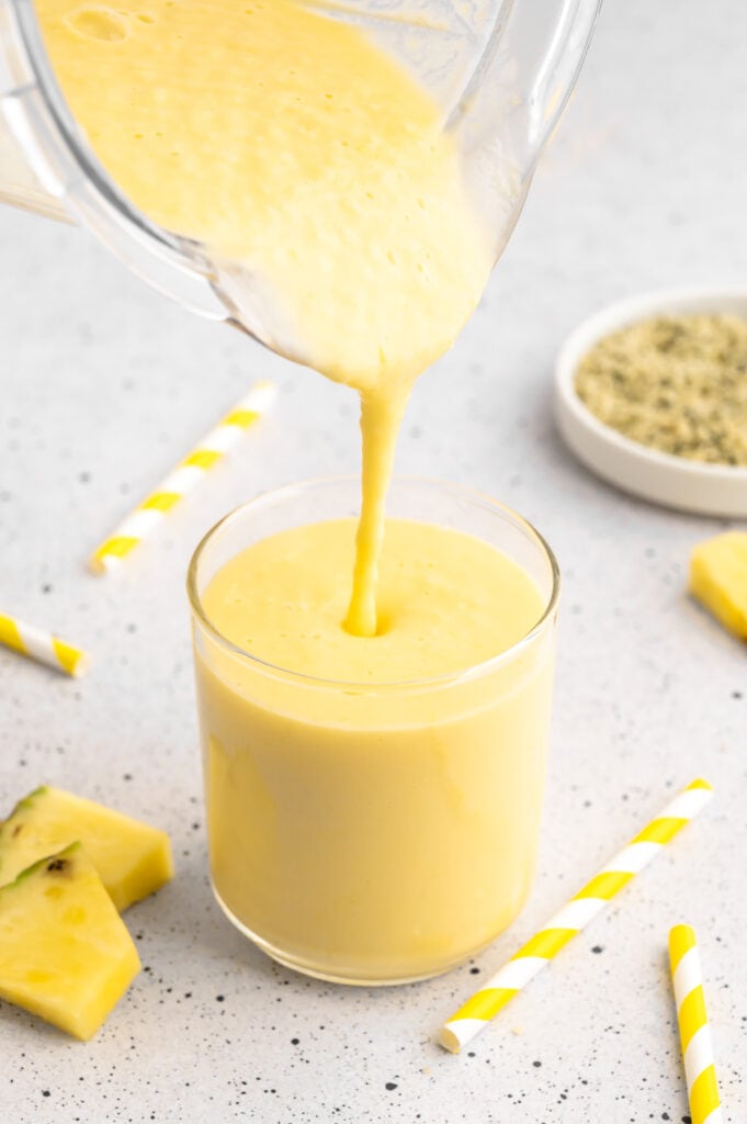 a pitcher of mango pineapple smoothie pouring into a glass of smoothie