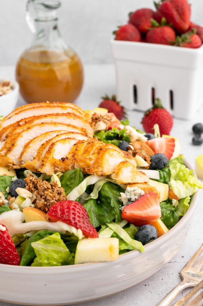 up close picture of market salad with chicken on top with strawberries and the dressing in the background