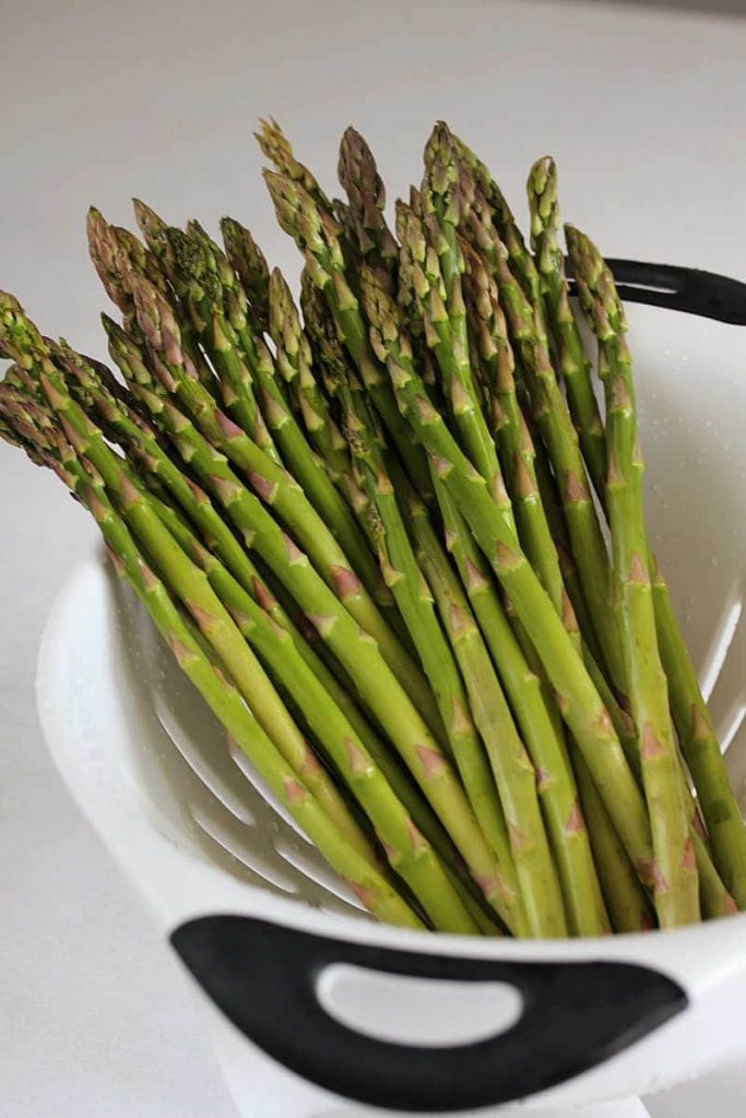 Wash a bunch of asparagus in a white strainer