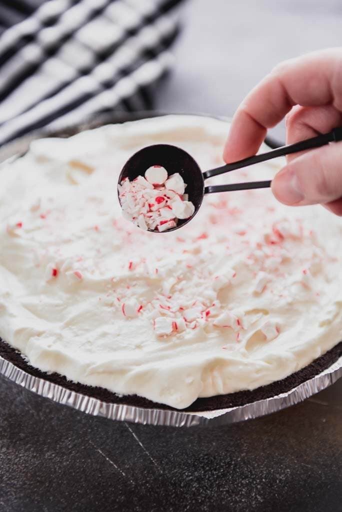 An oreo pie with a woman pouring crushed candy canes onto top of pie