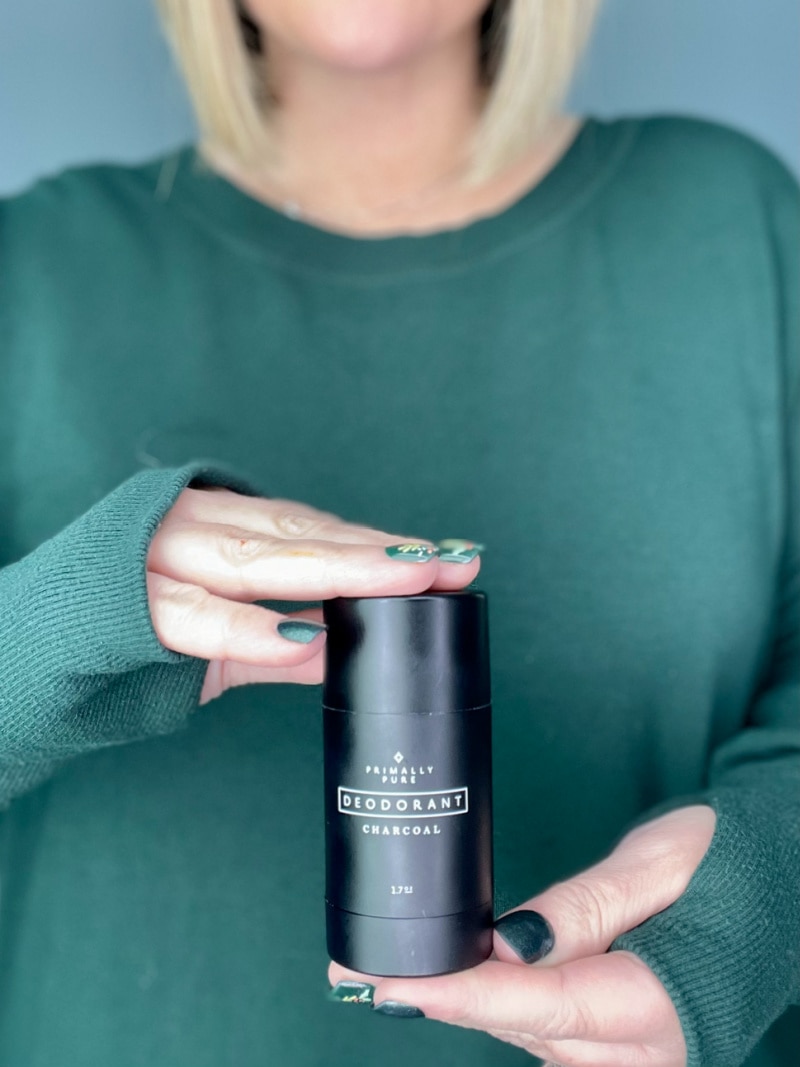 a woman in a green shirt holding a bottle of primally pure deodorant