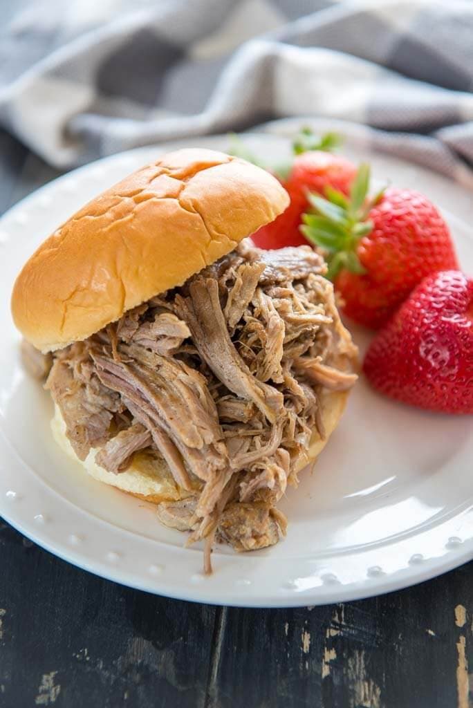 White plate with a easy slow cooker pulled pork sandwich and strawberries