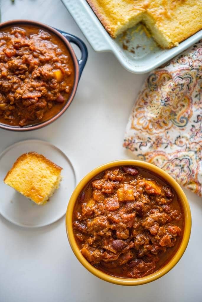 Overhead shot of 2 bowls of Pumpkin Chili and a piece of cornbread that is cut and a pan of cornbread.