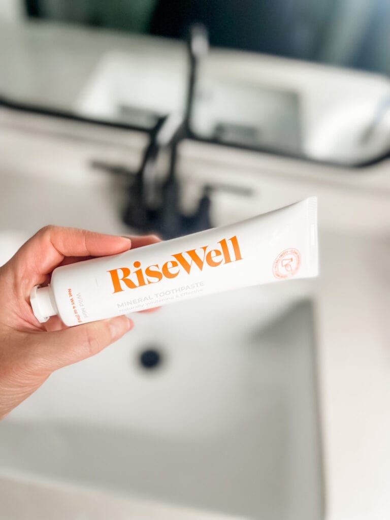 a woman holding a bottle of RiseWell toothpaste above her bathroom sink