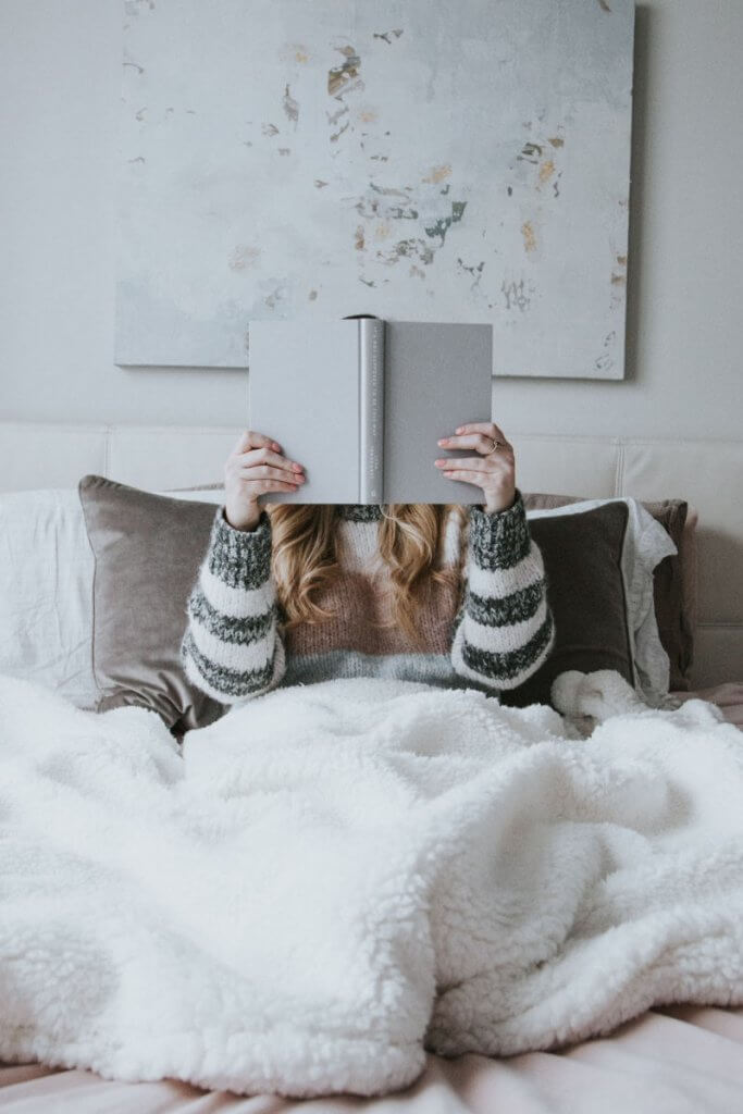 a woman in bed holding a book that is covering her face