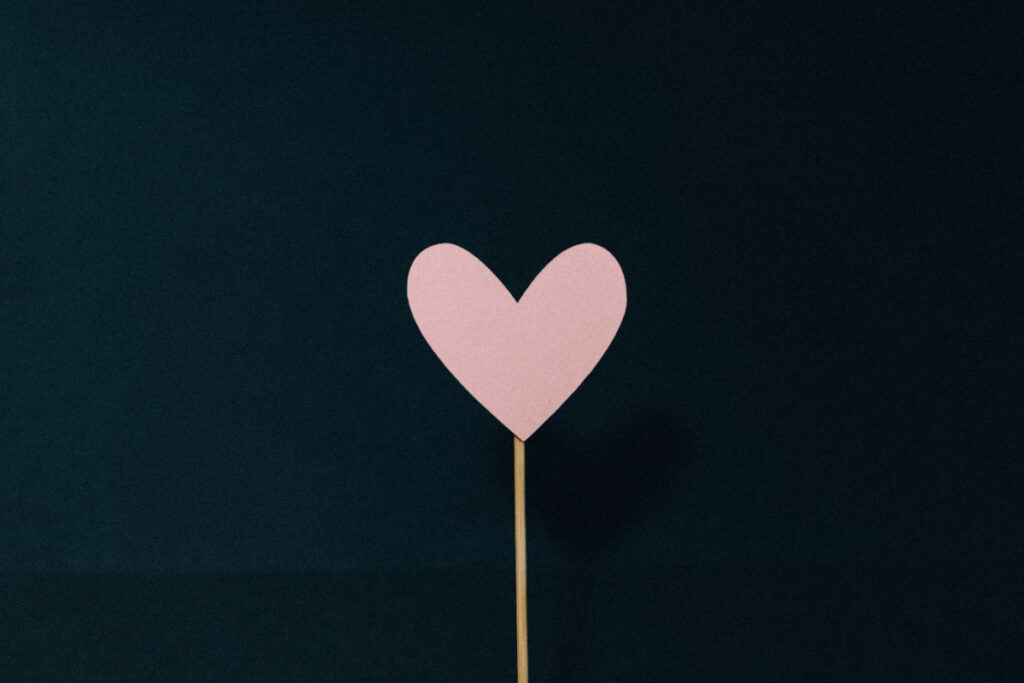a black picture with a single pink heart on a wooden stick