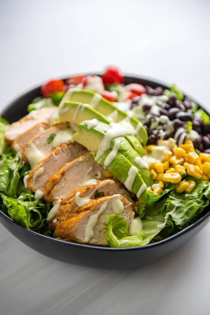 bowl of salad with chicken, avocado, beans, corn and tomatoes drizzled with dressing