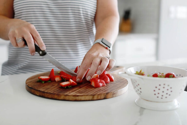 a woman cutting strawberries on a wooden cutting board