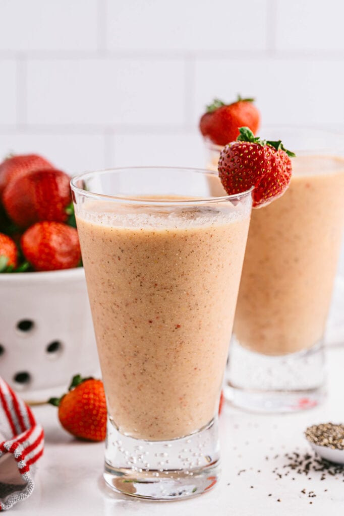 close up photo of two cups of strawberry mango smoothie with strawberries behind them
