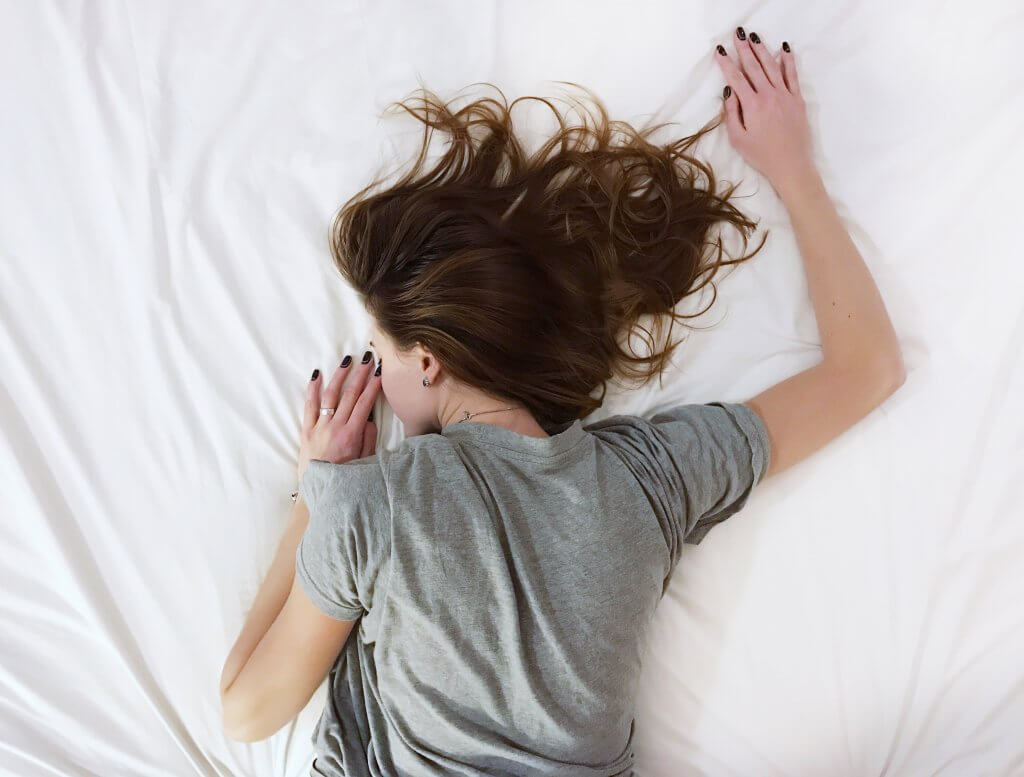 Woman laying on bed in a grey t-shirt and brown hair