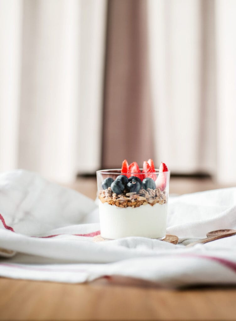 a glass jar of yogurt with granola and berries on a napkin on a table