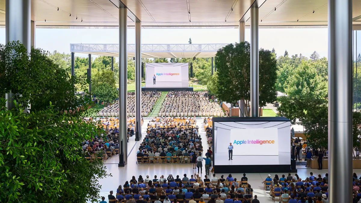 Apple WWDC 2024 attendees sit in chairs in front of a dias and two screens showing the words "Apple Intelligence."