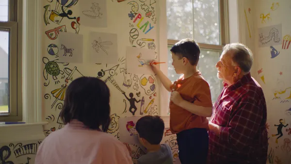 Two adults watch two children draw in an art-filled room