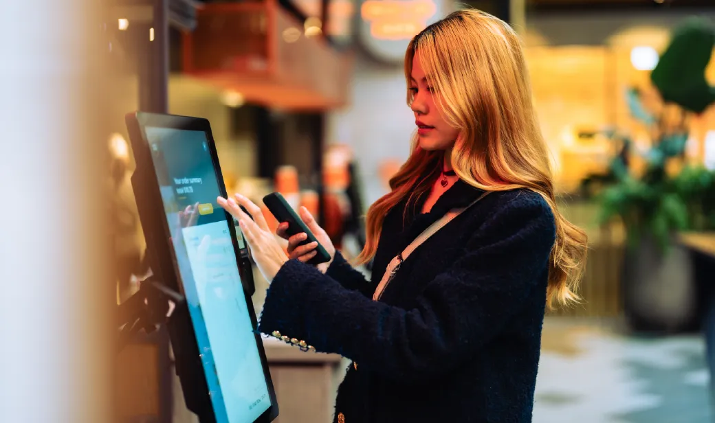 Women in casual clothing paying using automatic payment machine and smartphone.