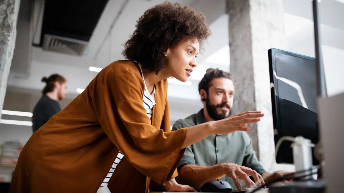 A pair of coworkers look at a computer screen