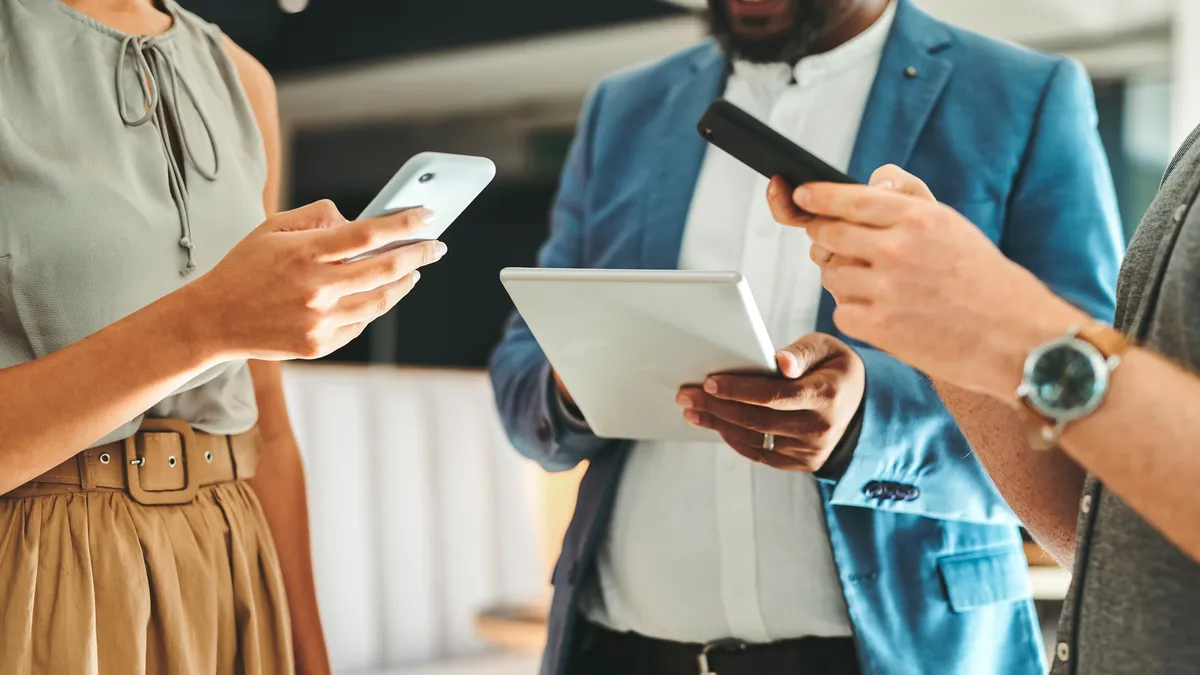 man with a notebook and 2 women with cell phones in a half circle talking